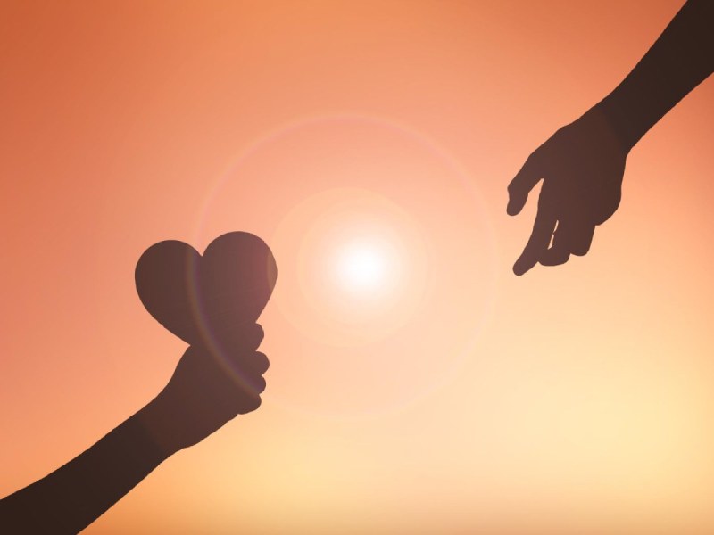 silhouette hands with heart shape against orange sky